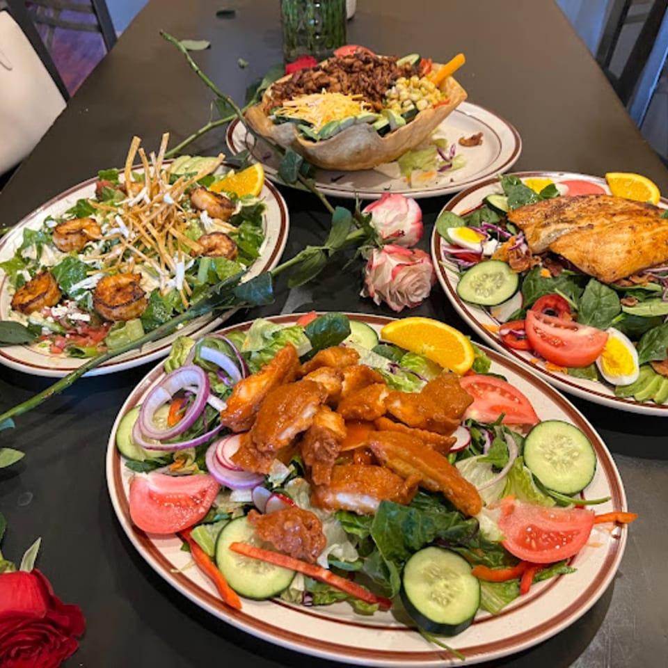 Four vibrant Mexican salads, including a taco salad, shrimp salad, and chicken salad, on a dark table.