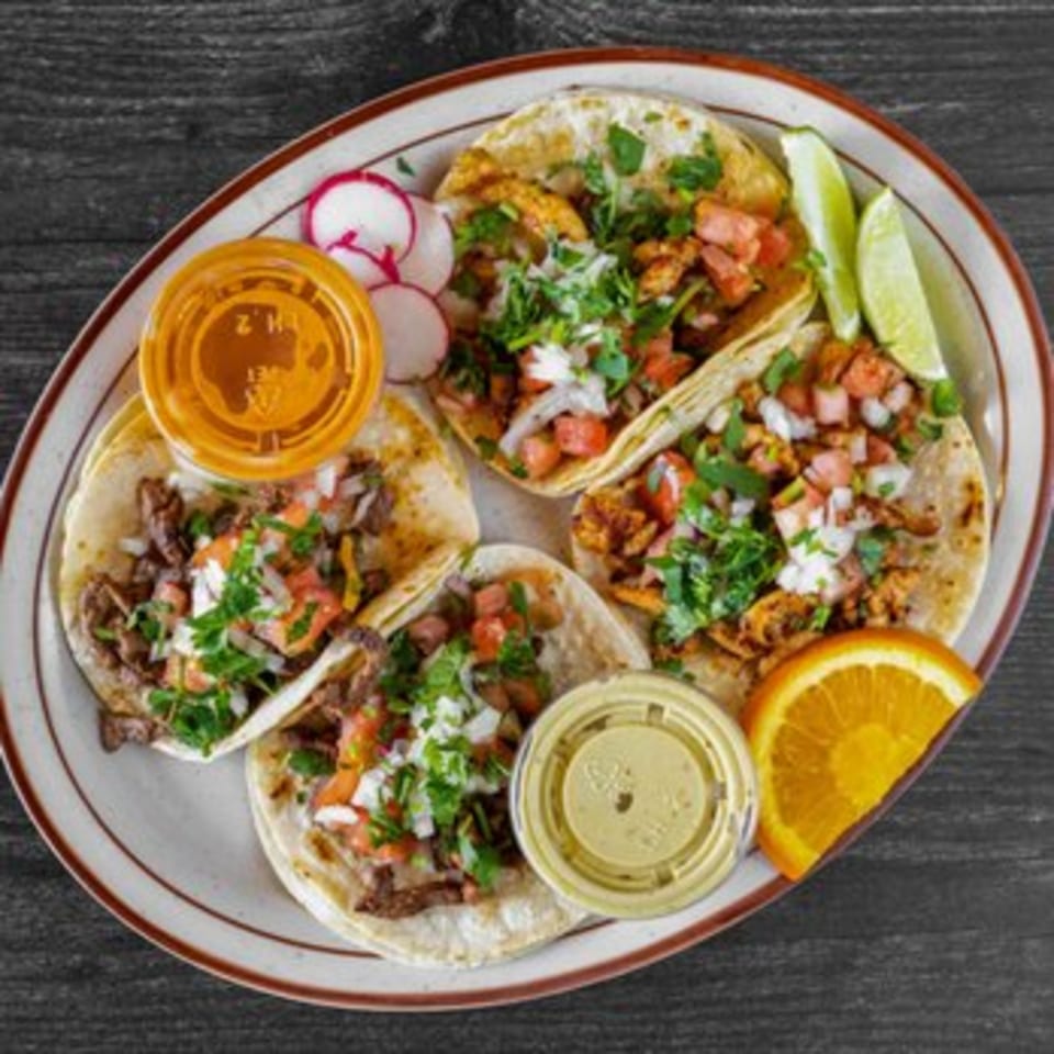 Four Fiesta Bowl tacos with meat, pico de gallo, cilantro, lime, radish, orange slice, and sauces.