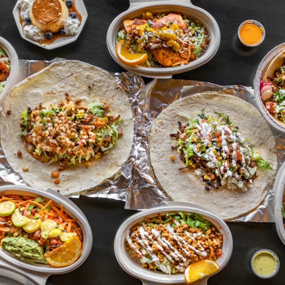 Overhead view of Fiesta Bowl's Mexican food spread, including burritos, bowls, and flan dessert.