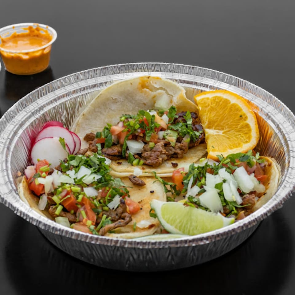 Three Fiesta Bowl Mexican street tacos with meat, pico de gallo, radishes, and citrus in a foil container.