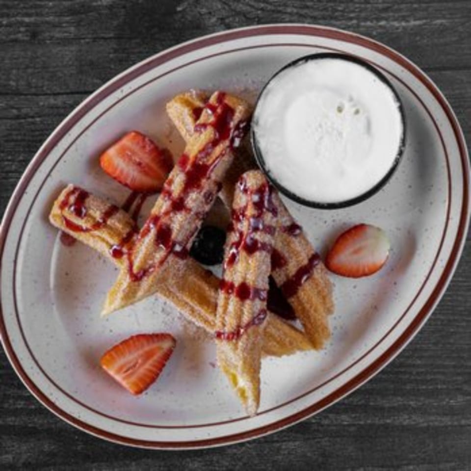 Churros drizzled with strawberry sauce, powdered sugar, fresh strawberries, and whipped cream.
