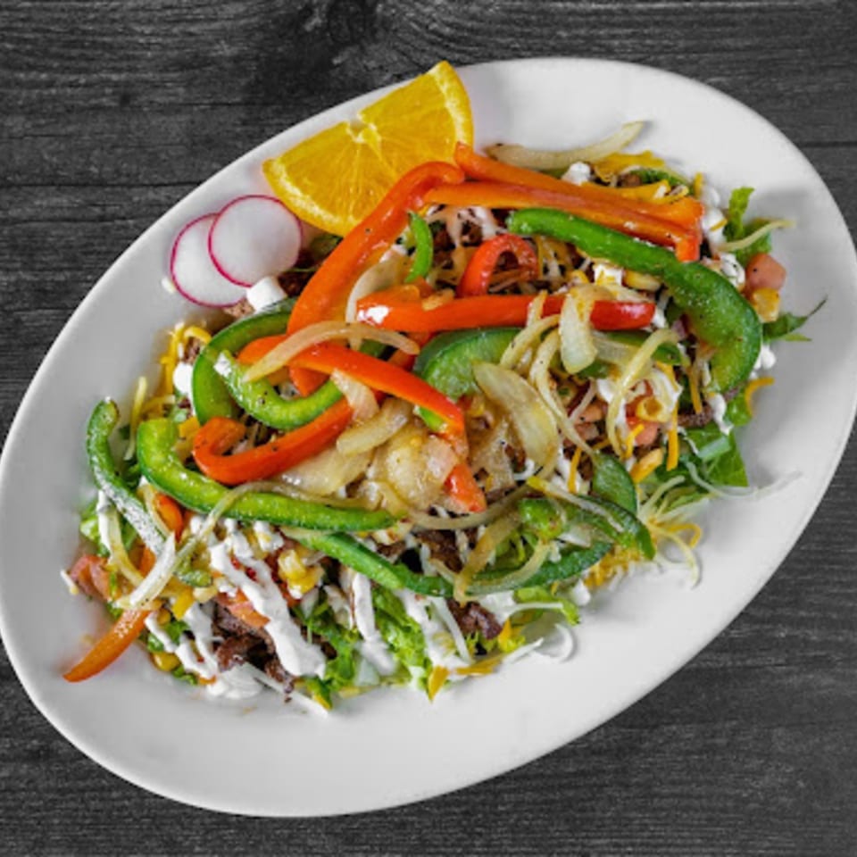 A vibrant Fiesta Bowl fajita salad with grilled peppers, onions, and a citrus slice on a white plate.