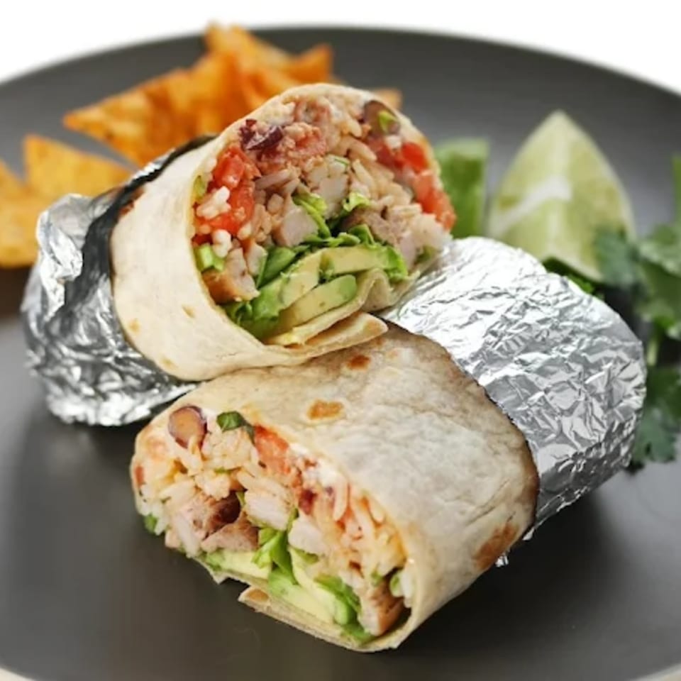 Two halves of a Fiesta Bowl burrito, filled with chicken, rice, avocado, and lettuce, on a dark plate.