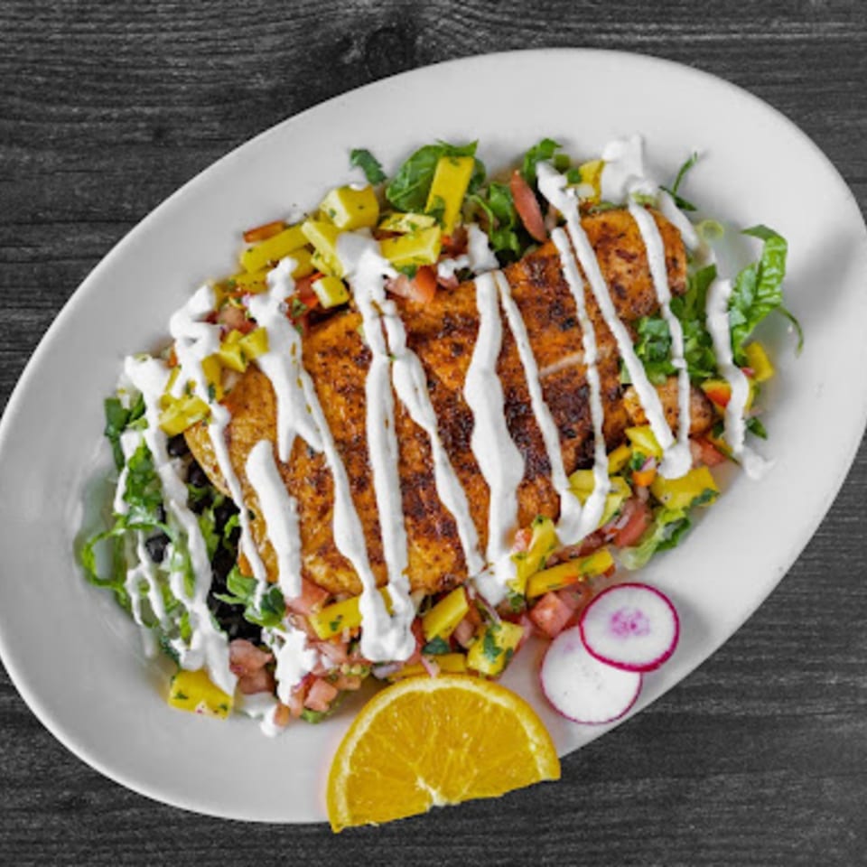 Fiesta Bowl's grilled chicken with mango salsa, lettuce, and crema on a white plate.